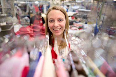 thrift store employee smiles as she puts clothes on a clothing rack